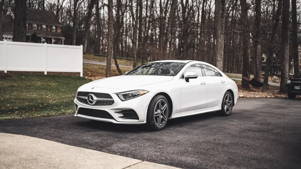 A sleek white Mercedes-Benz sedan parked on a driveway surrounded by a wooded area