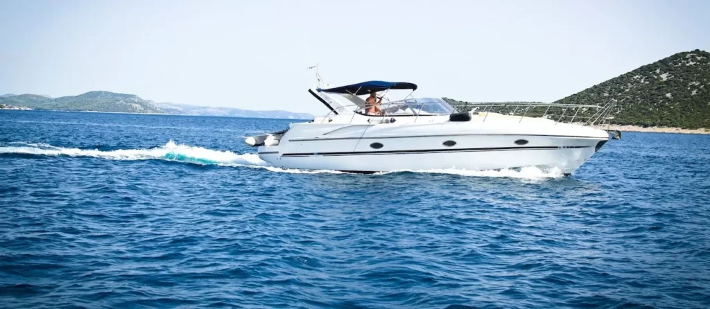 A sleek white yacht cuts through the open sea under a clear blue sky